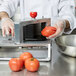 A person using a Vollrath Redco InstaSlice machine to slice tomatoes.