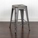 A Flash Furniture distressed silver metal counter height stool with a drain hole seat on a wood floor.