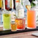 A row of Acopa Madras Rocks glasses filled with different colored drinks on a cocktail bar.