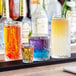 A table in a cocktail bar with a group of Acopa Gardenia rocks glasses filled with different colored liquid.