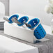 A Steril-Sil stainless steel flatware organizer with blue perforated plastic cylinders holding silverware on a table.