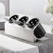 A Steril-Sil stainless steel flatware organizer with black perforated cylinders holding silver and black utensils.