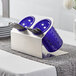 A Steril-Sil stainless steel flatware organizer with purple perforated plastic cylinders holding utensils.