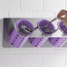 A hand placing a spoon into a violet Steril-Sil cylinder in a flatware organizer.