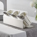 A Steril-Sil stainless steel flatware organizer with white cylinders holding spoons and forks.