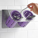 A hand holding a spoon and a Steril-Sil stainless steel flatware organizer with violet plastic cylinders containing utensils.
