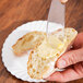 A person's hand using a Fineline clear plastic sandwich spreader to spread butter on a piece of bread.