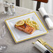 A Visions white plastic plate with gold bands holding a plate of food with a lemon wedge on top.