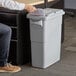 A person in jeans putting a paper in a white Rubbermaid Slim Jim trash can with a confidential document lid.