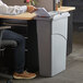 A person sitting at a desk with a paper in a Rubbermaid Slim Jim trash can.