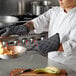 A woman in a chef's uniform uses San Jamar Bestguard oven mitts to cook food in a pan.