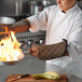 A chef in a white uniform using San Jamar Bestguard oven mitts to hold a pan with flames.