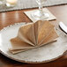 A plate with a folded Hoffmaster Linen-Like Natural Dinner Napkin on it.