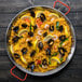A Matfer Bourgeat carbon steel paella pan filled with rice and seafood with lemon wedges.