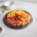 A Visions clear plastic catering tray with a lid holding a variety of fruit on a table.