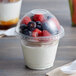 A clear plastic squat cup of yogurt with berries.