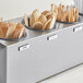 A stainless steel flatware organizer with wooden spoons and forks in perforated stainless steel cylinders.