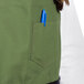 A person wearing a green Uncommon Chef apron with black webbing and using a blue pen in a pocket.