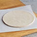 A round white Rich's pizza dough on a white paper on a wooden surface with a knife.