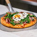 A pizza with egg and greens being cut on a table with a spatula.