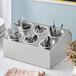 A stainless steel flatware organizer with perforated plastic cylinders holding silverware.