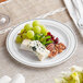 A Visions white plastic plate with silver bands holding a variety of food including cheese.