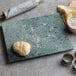 A green marble pastry board with dough, a rolling pin, and cookie cutters.