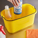 A hand using Kleary cleaning supplies to clean a yellow Rubbermaid pail.