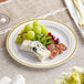 A Visions white plastic plate with gold bands holding cheese and grapes on a table with more food.