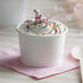 A white paper cup filled with frozen yogurt and sprinkles.