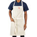A man wearing a sand beige Uncommon Chef apron with natural webbing and red pockets.