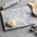A Fox Run white marble pastry board with dough and a rolling pin.