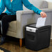 A woman sitting on a couch using a black and silver GBC ShredMaster paper shredder.