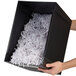 A person holding a black box with shredded paper.