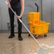 A person using a Carlisle Sparta stainless steel mop handle to clean a floor.