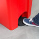 A person's shoe stepping on a red Continental rectangular step-on trash can.