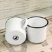 Two white Crow Canyon Home enamelware mugs with black rims on a table.