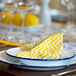 A close up of a Crow Canyon Home white enamelware plate with a blue rim with a yellow and white napkin on it.
