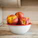 A bowl of peaches in a Crow Canyon Home enamelware bowl with a red rim on a table.