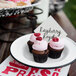 A cupcake with raspberry and cream frosting on a Crow Canyon Home white enamelware plate with black rolled rim.