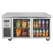A Turbo Air undercounter refrigerator with two glass doors full of fruit and juice.