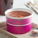 A pink Choice paper food cup filled with soup on a tray.