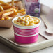 A table with a tray of a pink Choice paper cup filled with macaroni and cheese and fries.