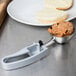 A Vollrath gray squeeze handle disher with food in it next to a plate of bread.