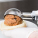 A person using a Vollrath gray metal scoop to dish ice cream onto a sandwich.