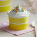 A yellow paper cup filled with ice cream and sprinkles with a spoon in it.