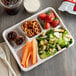 A white Huhtamaki Chinet cafeteria tray with compartments filled with food including salad, a drink, and a snack.
