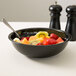 A black Cambro round ribbed bowl filled with fruit with a spoon in it on a table.