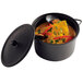 A Solia black plastic cooking pot with a lid filled with soup.