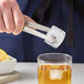 A person using Carlisle stainless steel ice tongs to add ice to a glass of liquid.